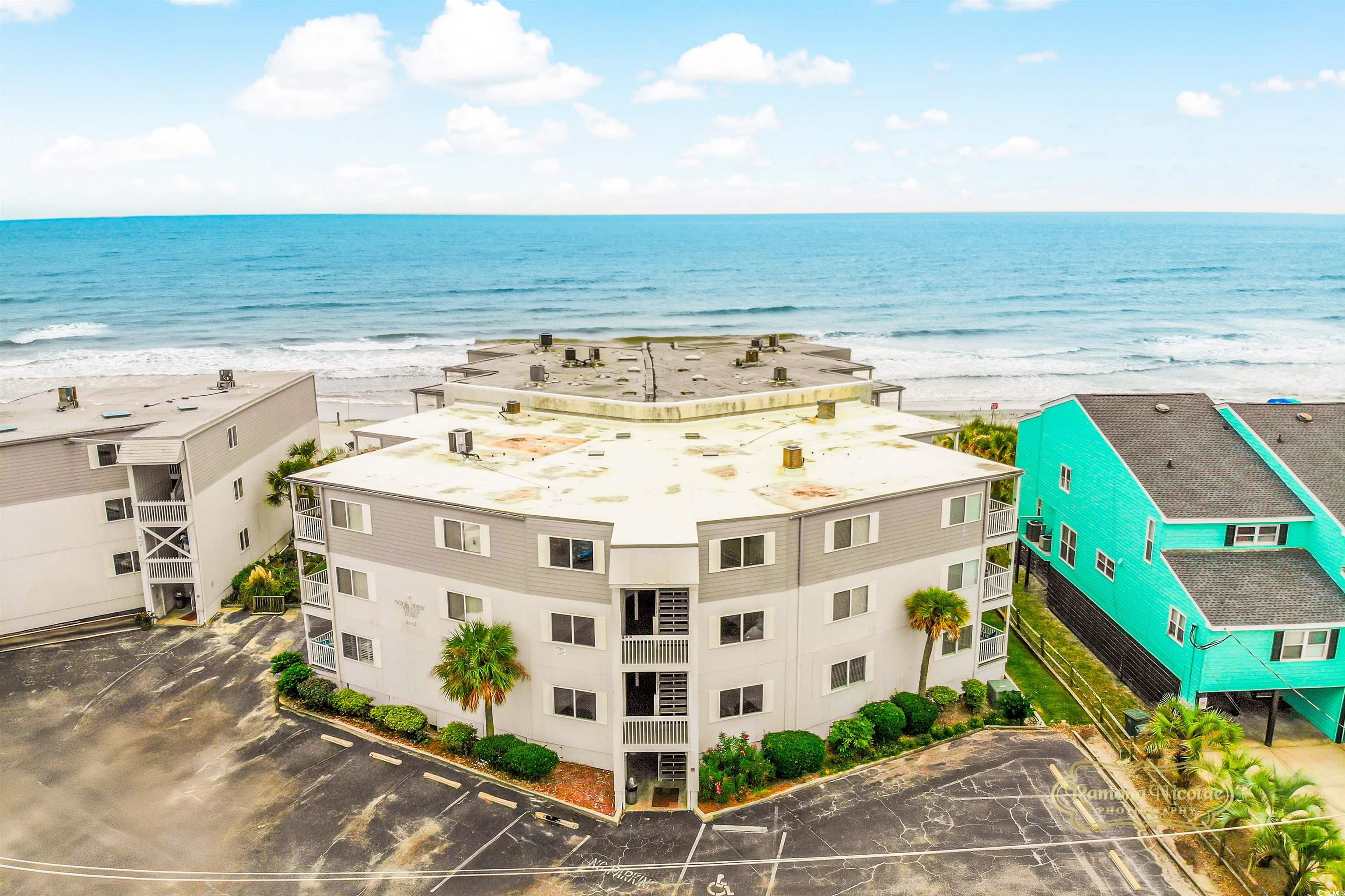 Beachfront condominium complex beside the Atlantic Ocean, viewed from above with neighboring buildings and parking.