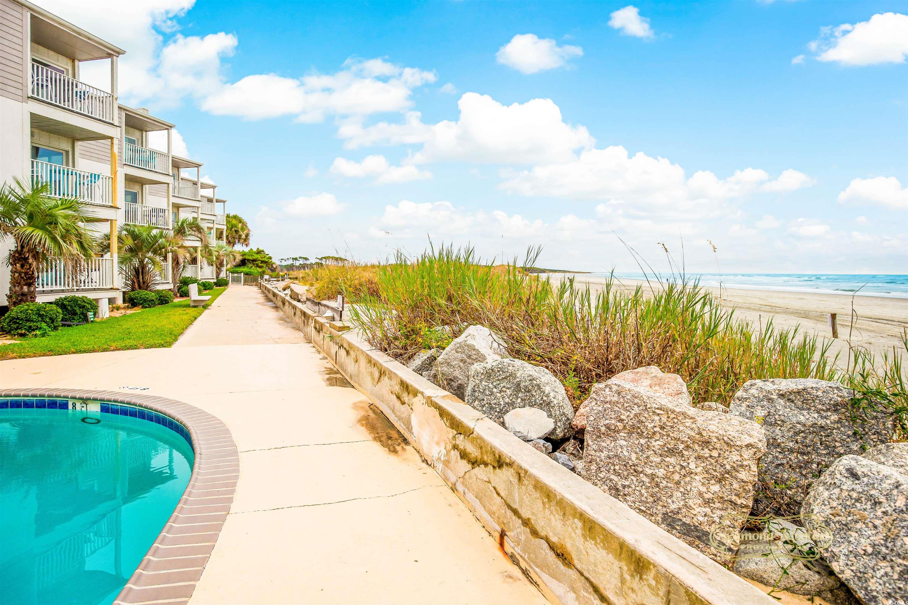Beachfront condominiums beside a pool, with dune grasses and ocean views.