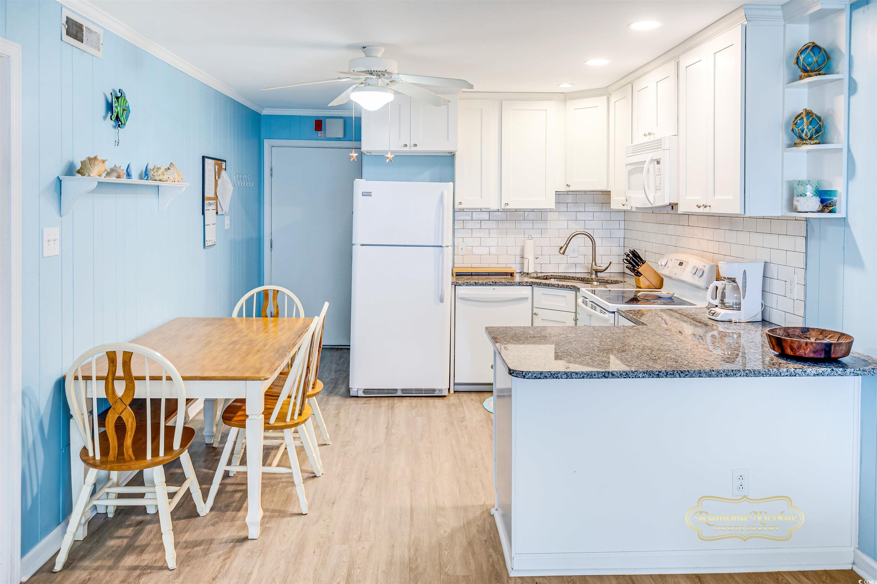 Condo kitchen with white cabinets, granite counters, and a dining table beside blue walls.