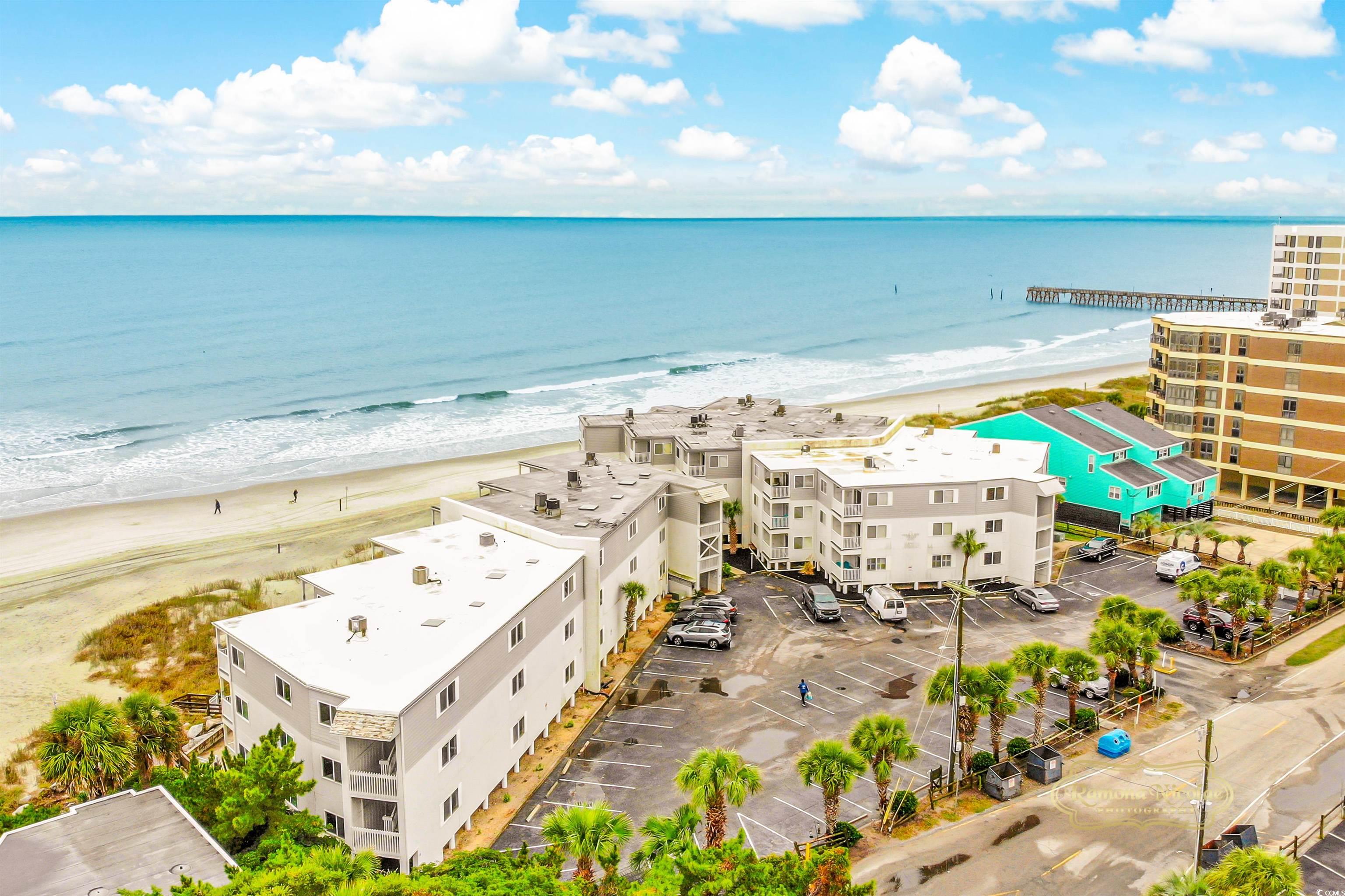 Aerial view of beachfront condominiums beside the sandy shore, with a pier extending over the ocean.