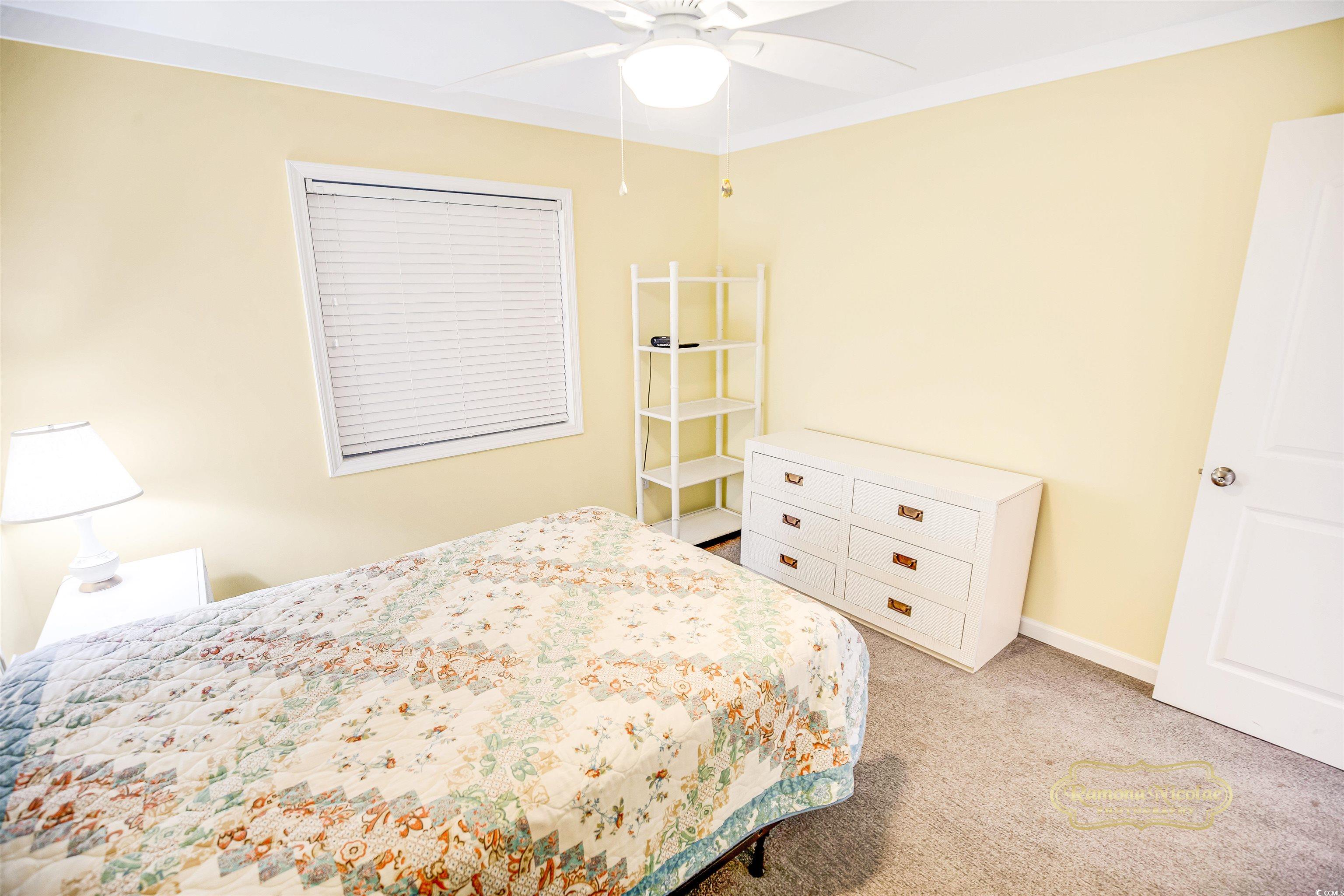 Bedroom with a floral quilt, pale yellow walls, white dresser, and ceiling fan.