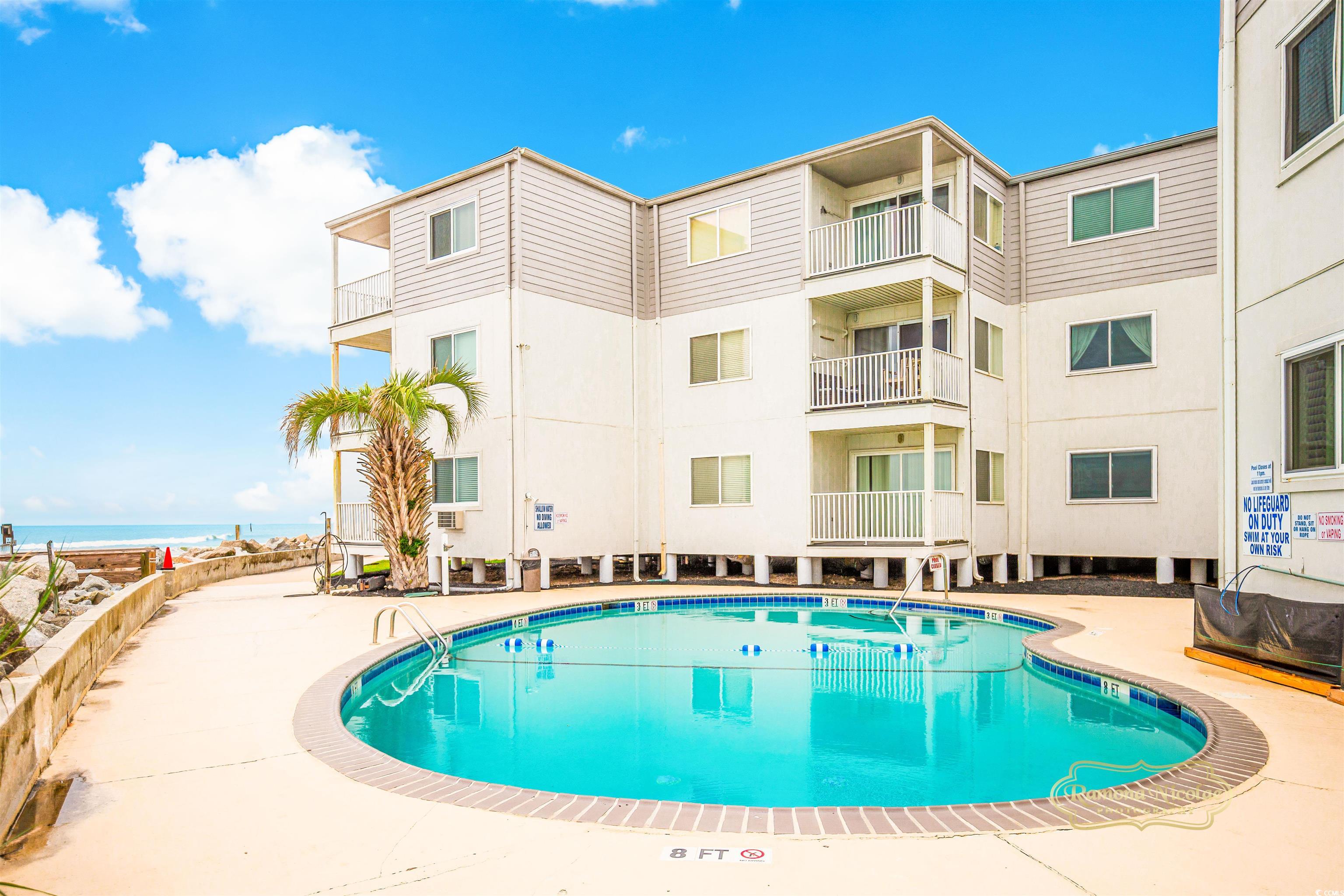 Outdoor pool beside a beachfront condominium, with the ocean visible beyond.