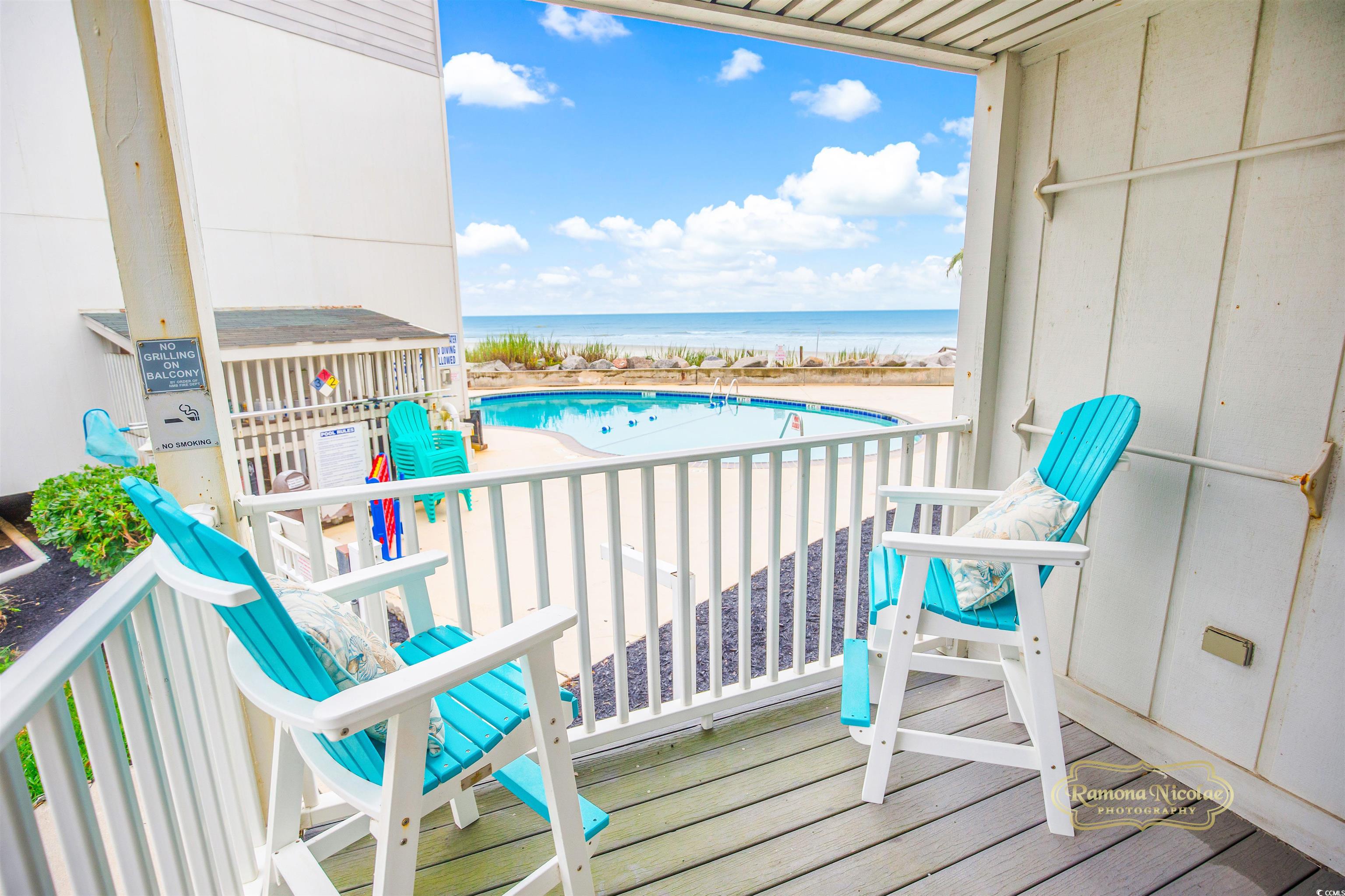 Condo balcony with turquoise chairs overlooking a swimming pool, beach and ocean.