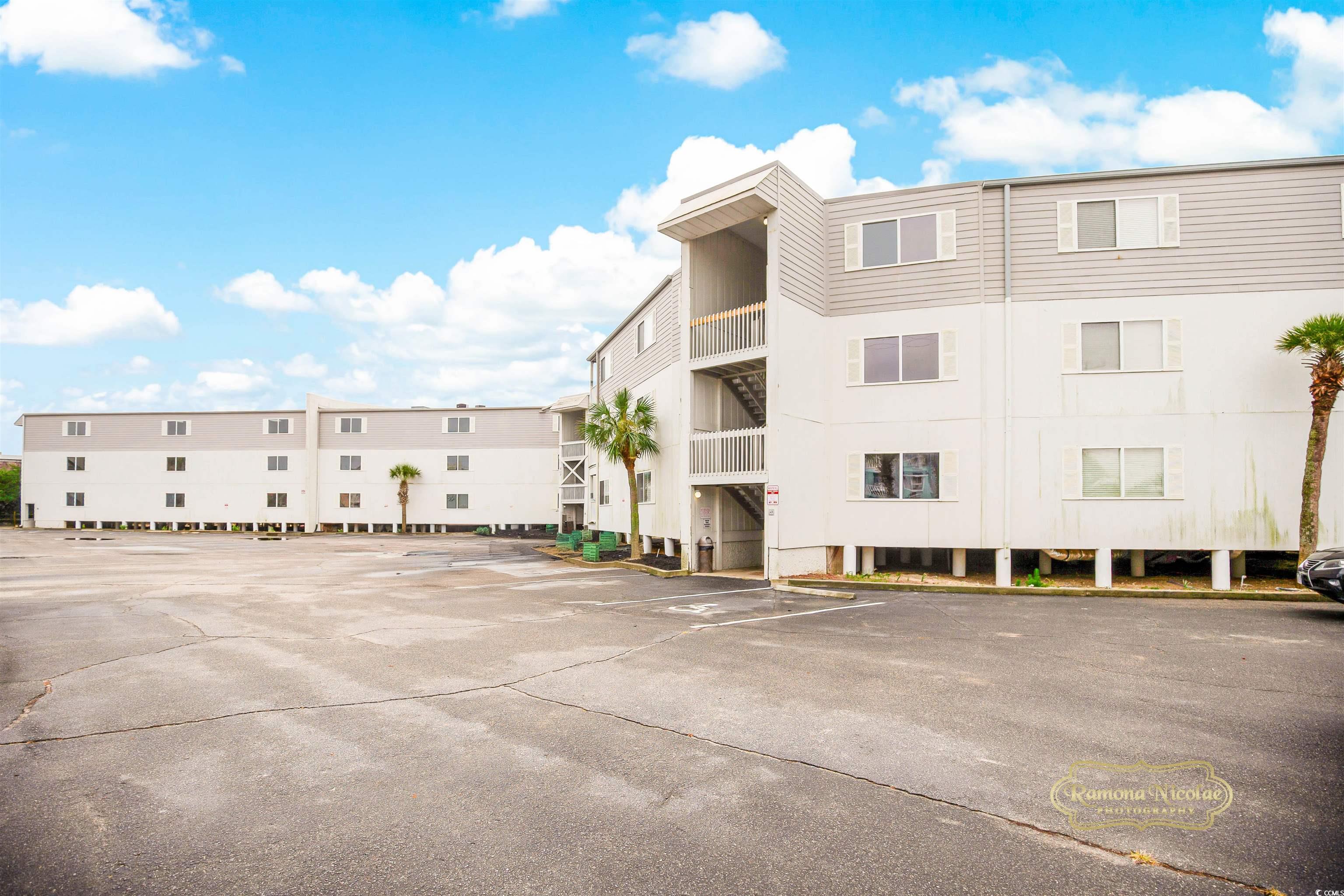 Multi-story condominium building with open stairwells and balconies beside a large parking lot.