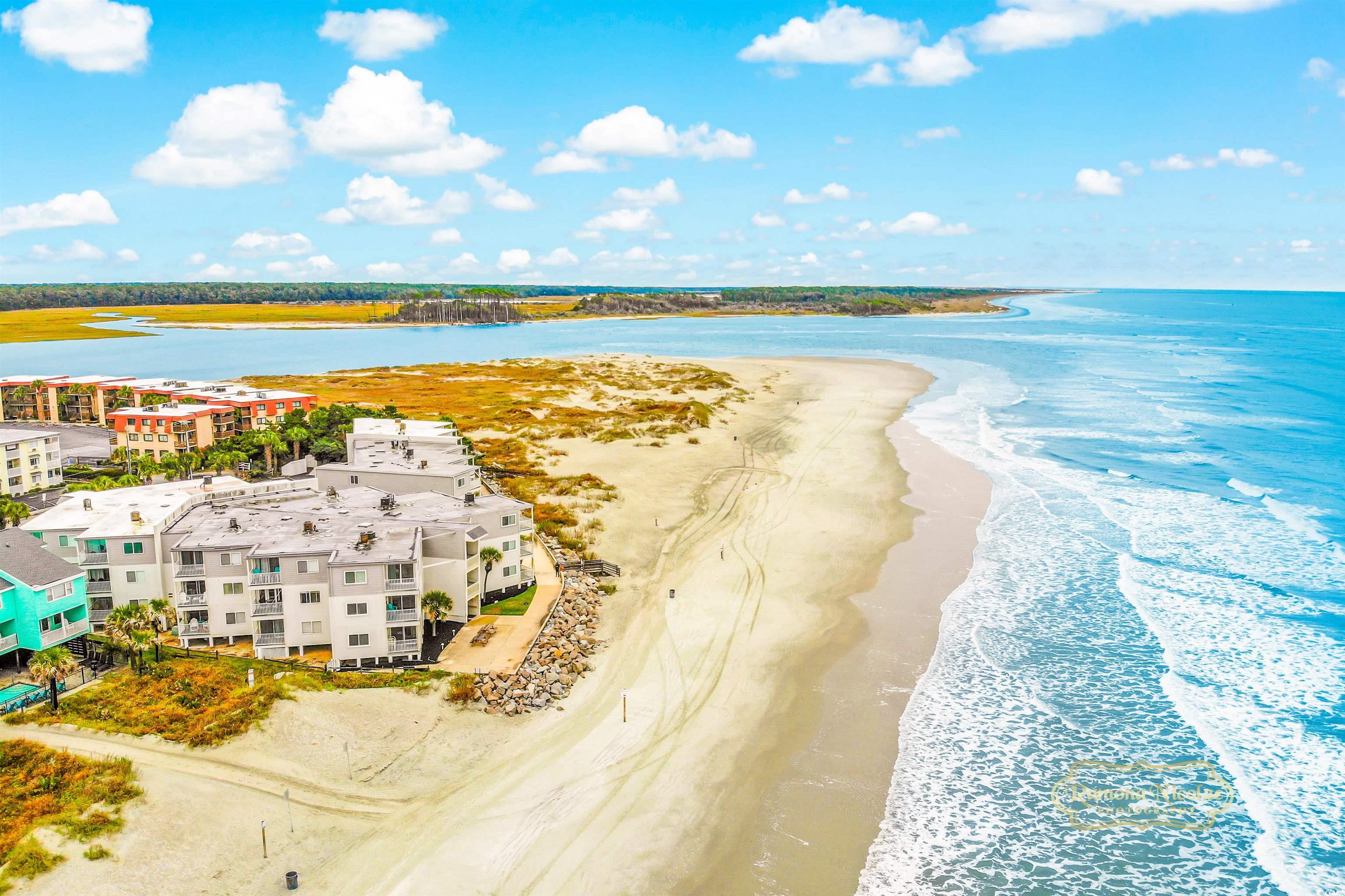 Aerial view of beachfront condos beside a broad sandy beach and curving ocean shoreline.