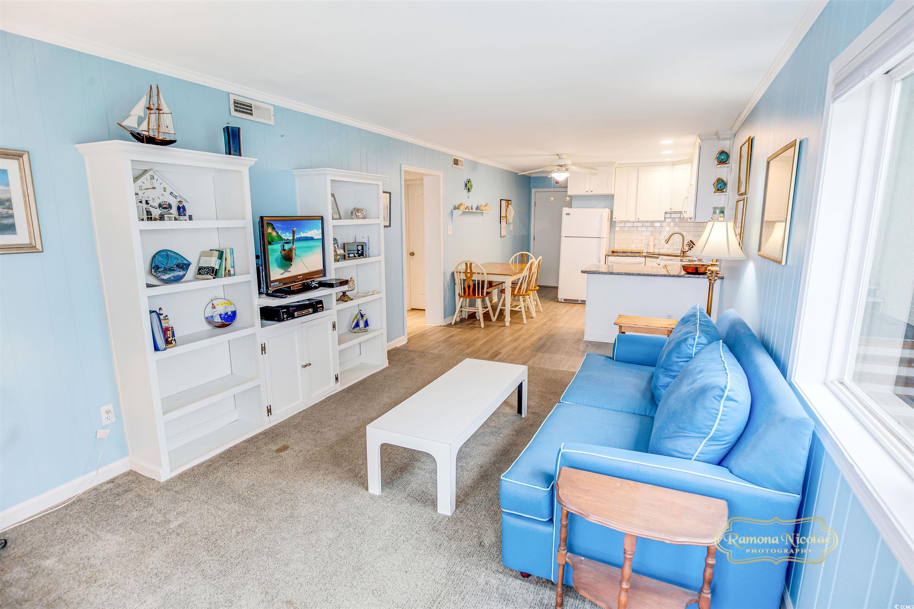 Coastal condo living room with a blue sofa, white built-ins, and an open kitchen.