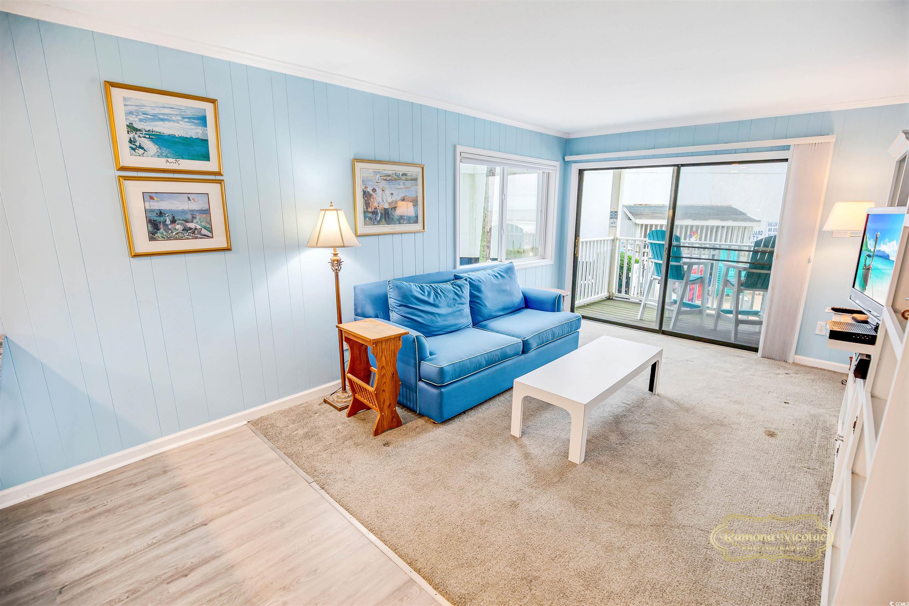 Condo living room with a blue sofa and sliding doors opening to a balcony with turquoise chairs.