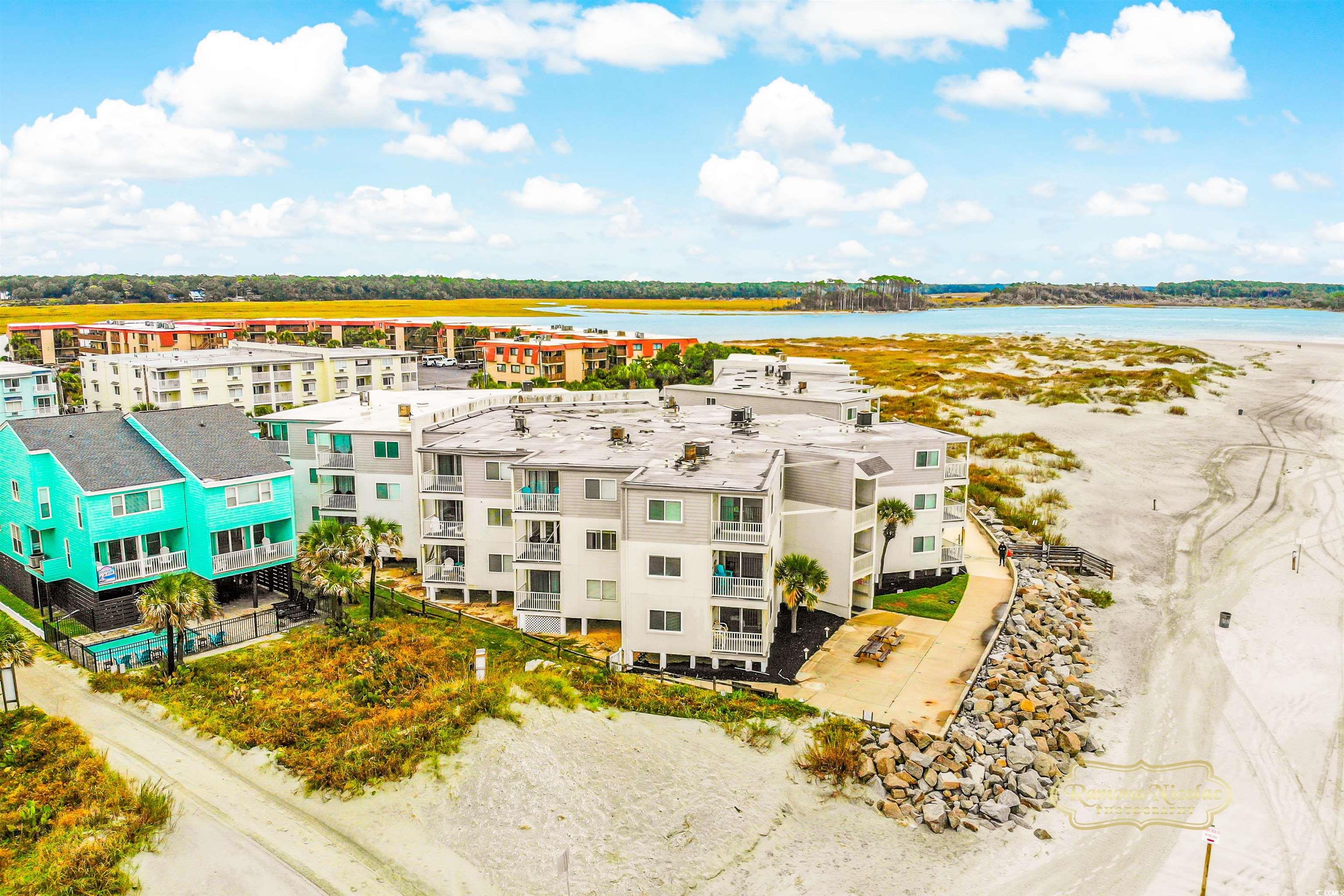 Beachfront condominiums beside a sandy beach, dunes, and coastal inlet.