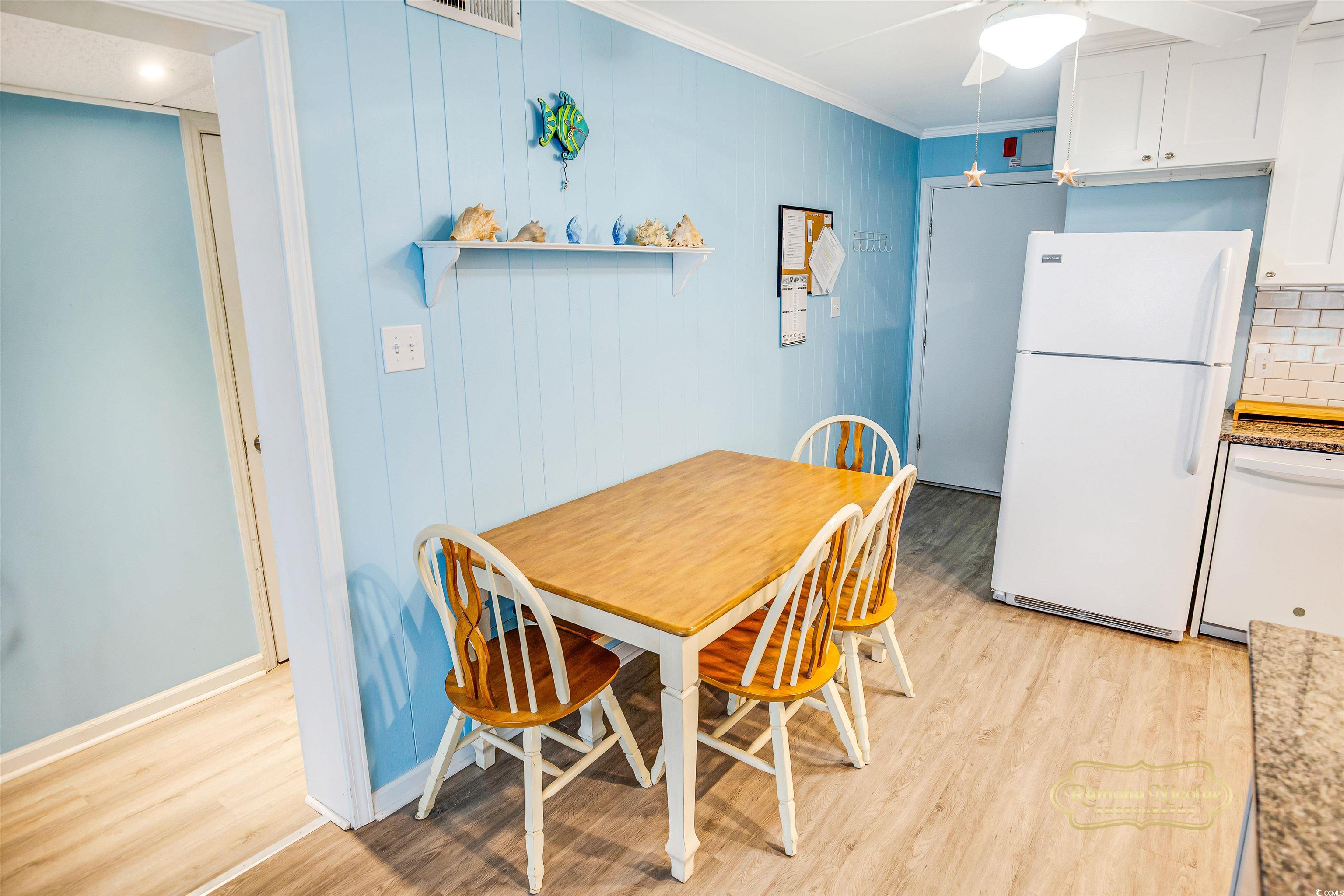 Condo dining area with a wooden table, white chairs, blue walls, and a refrigerator.