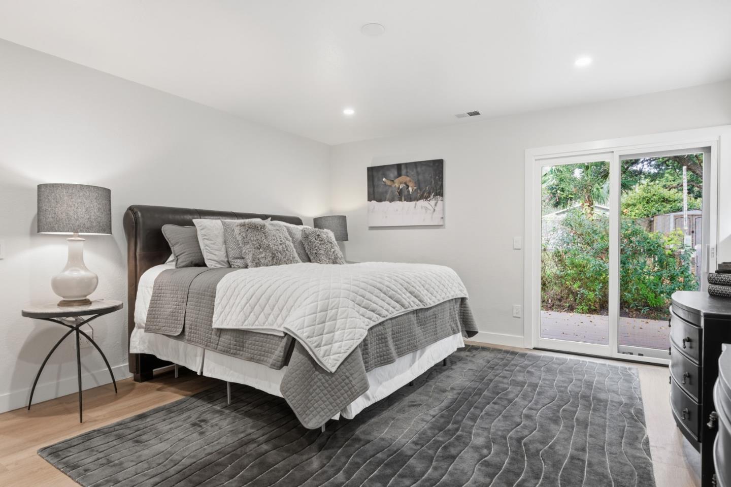 Bedroom with a layered gray-and-white bed and sliding glass doors overlooking greenery.