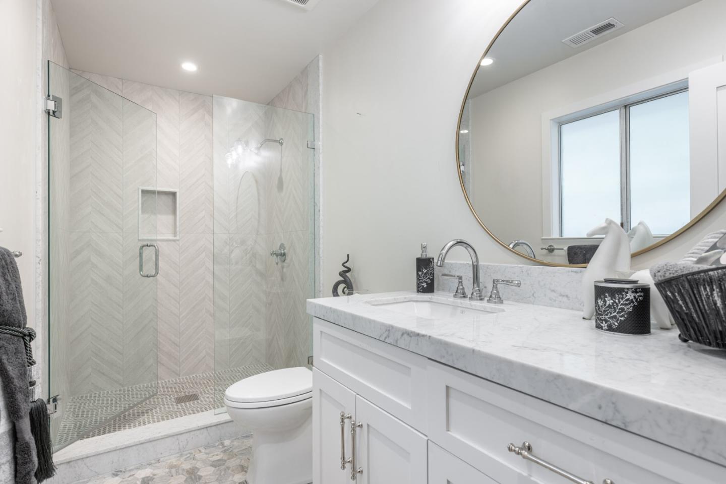 Bathroom with a glass walk-in shower, herringbone tile, and marble vanity.