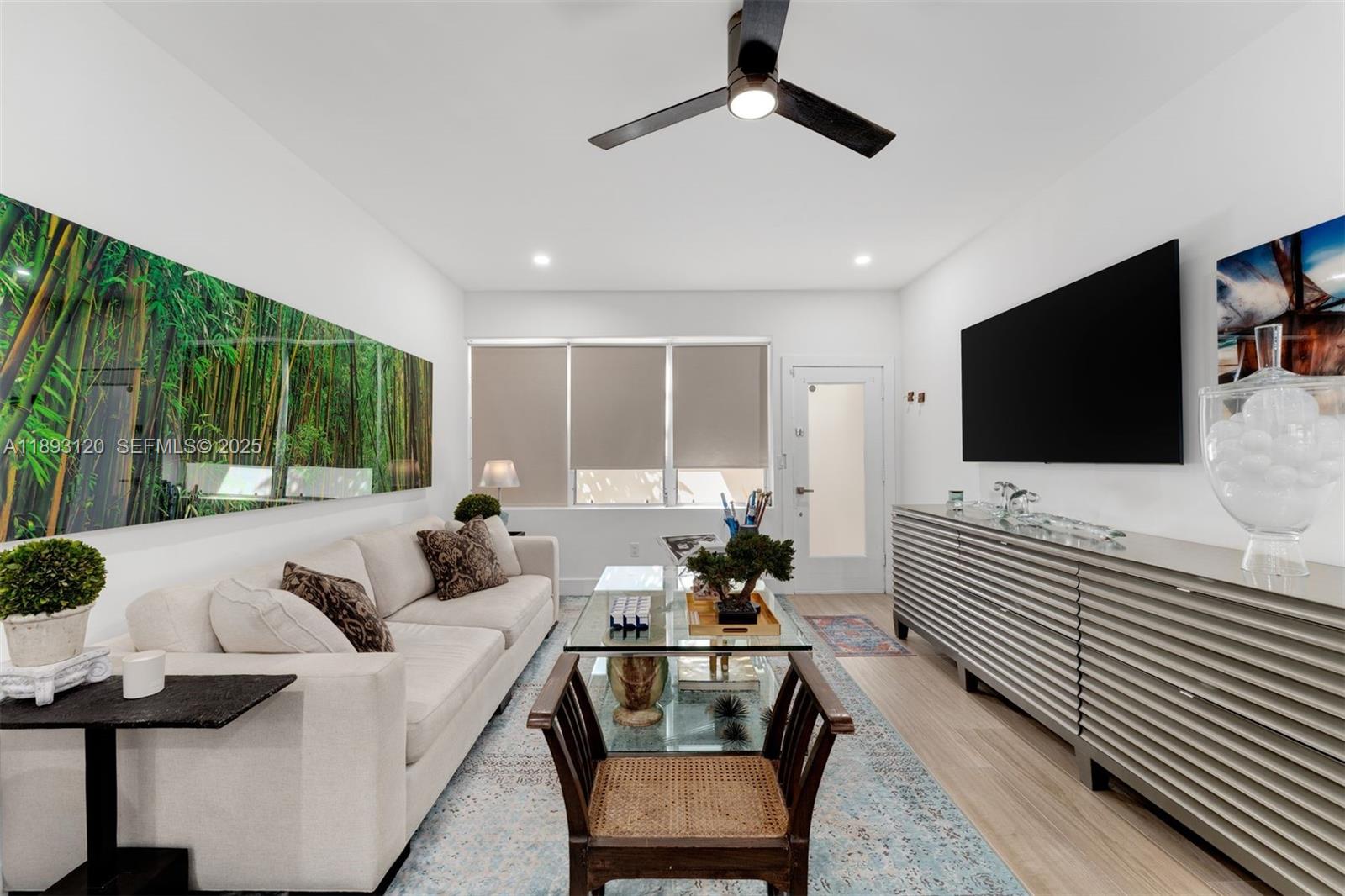 Living room with a white sectional, glass coffee table, bamboo mural, and wall-mounted television.
