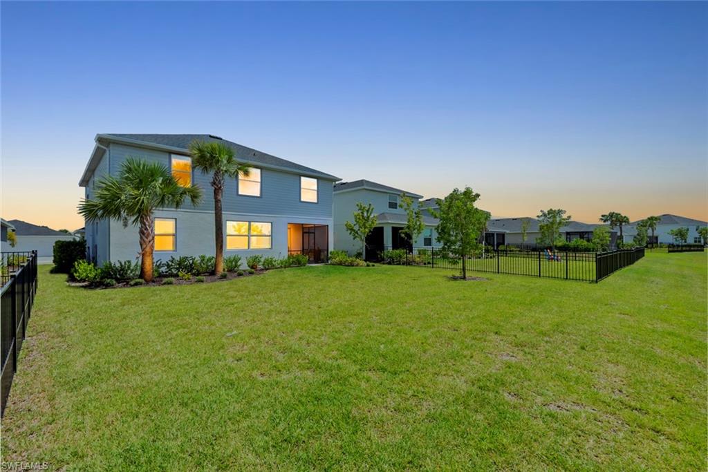 Two-story home with a broad fenced lawn, palm trees, and neighboring houses at sunset.