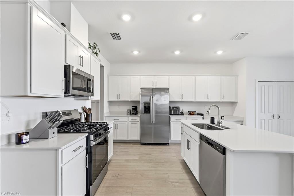 Kitchen with white cabinets, stainless steel appliances, gas range, and a large island with sink.