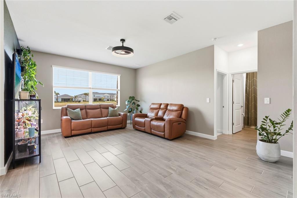 Living room with brown leather sofas, gray tile flooring, and a wide window overlooking neighboring homes.