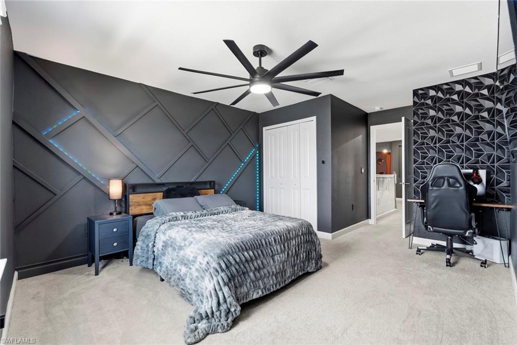 Bedroom with a geometric charcoal accent wall, upholstered bed, and gaming desk.