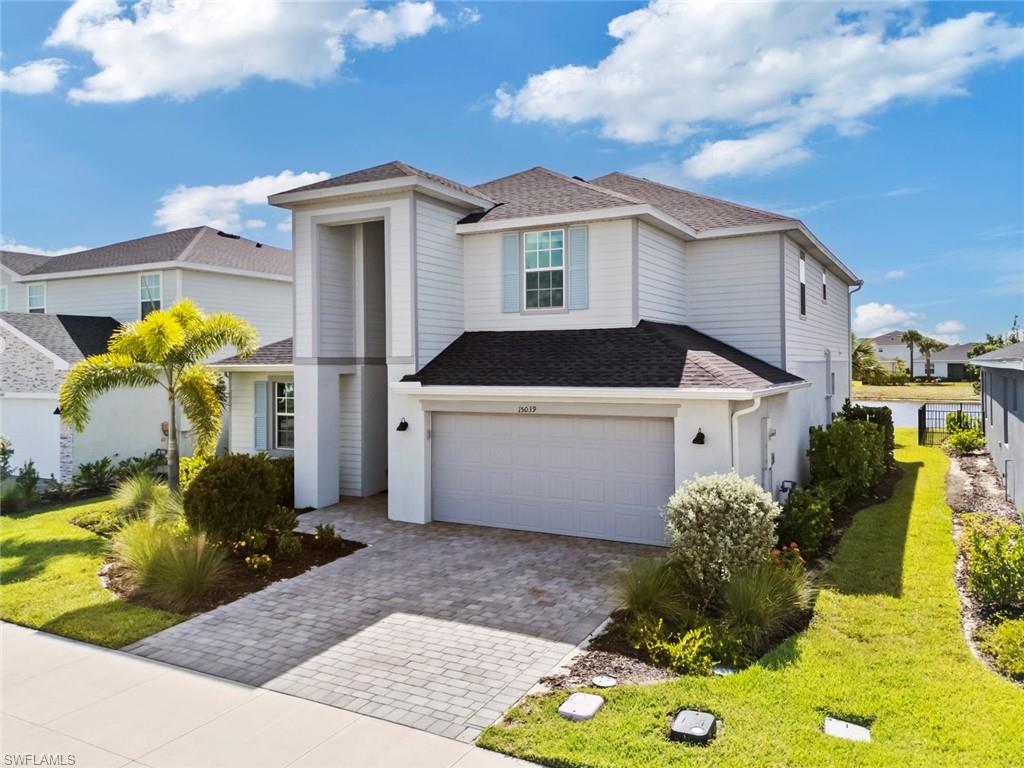 Two-story white house with a double garage, paver driveway, and landscaped front lawn.
