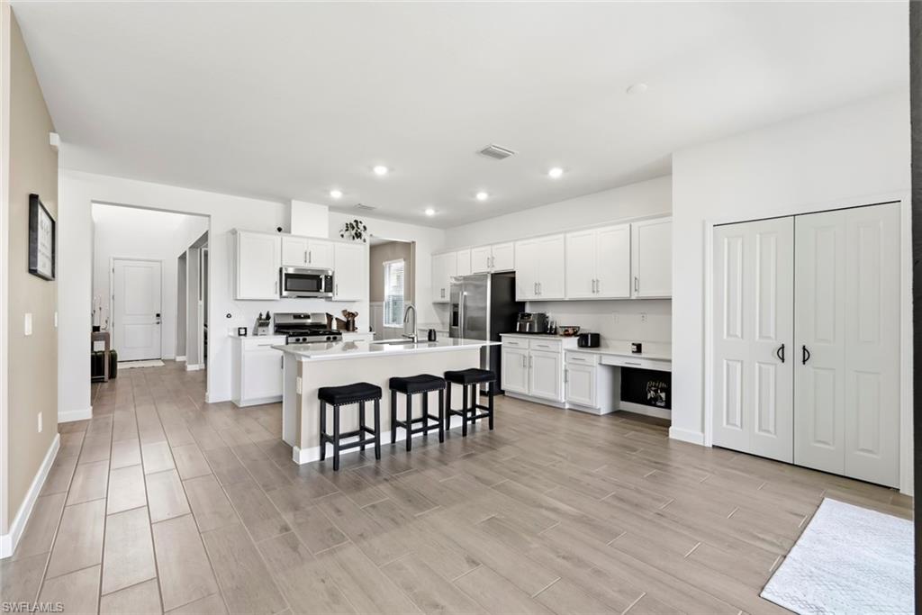 Open kitchen with white cabinets, stainless steel appliances, and a large island with three stools.