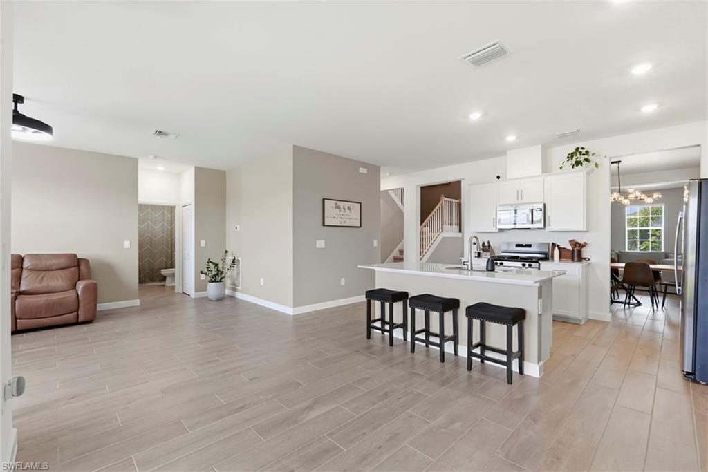 Open-plan kitchen with white island and black stools, adjoining a living area with a brown leather recliner.