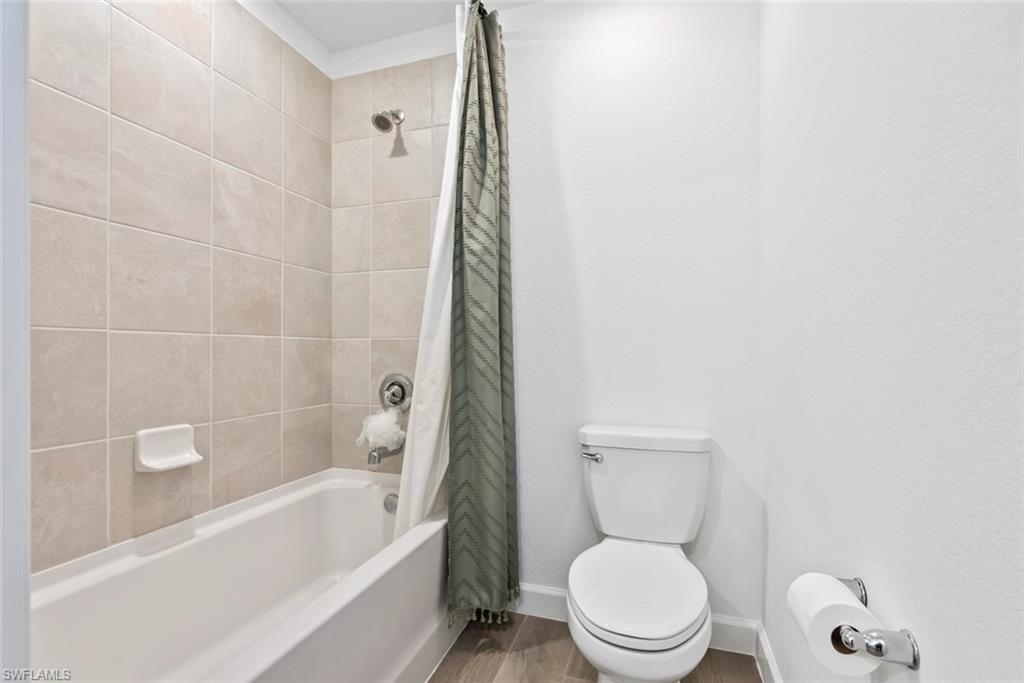 Bathroom with a white tub, beige tiled shower surround, patterned green curtain, and toilet.