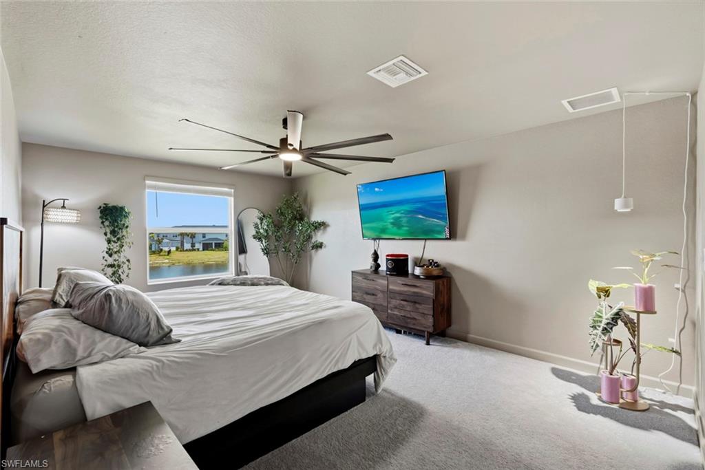 Furnished bedroom with a large bed, modern ceiling fan, and window overlooking water.
