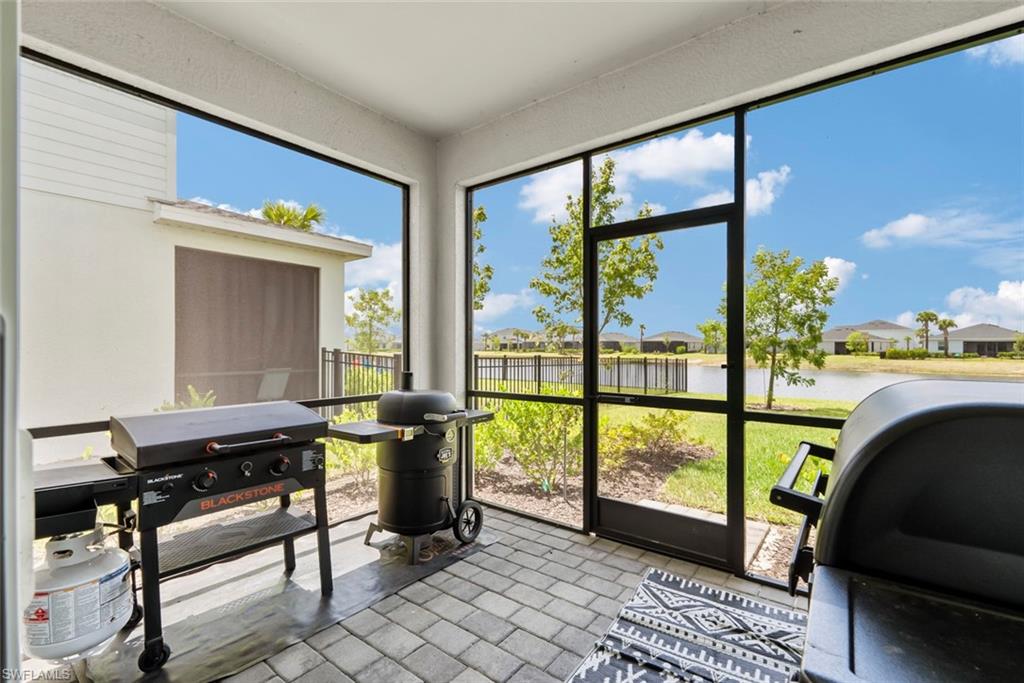 Screened lanai with two grills overlooking a pond and neighboring homes.