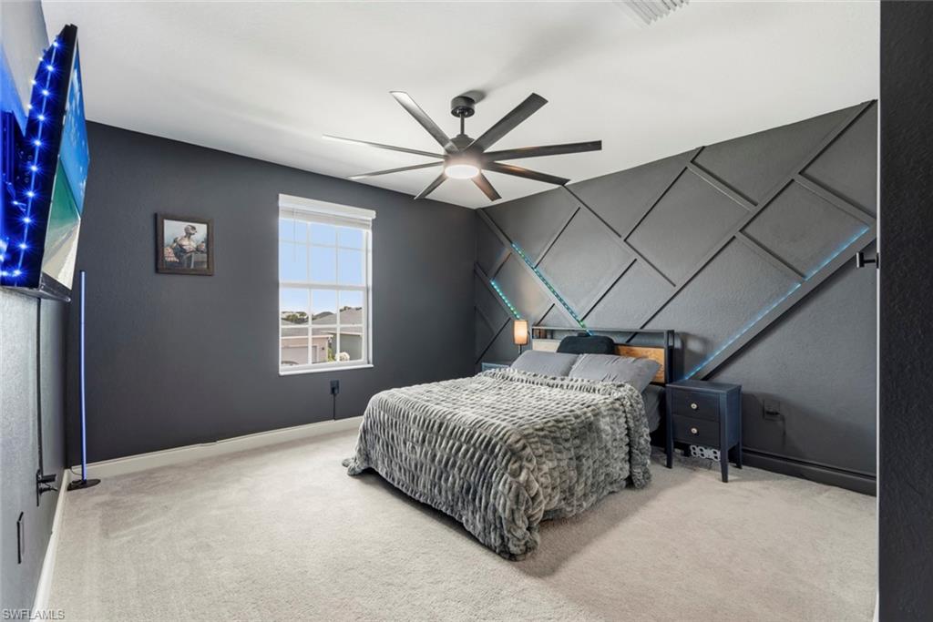 Furnished bedroom with a geometric gray accent wall, blue accent lighting, and a ceiling fan.