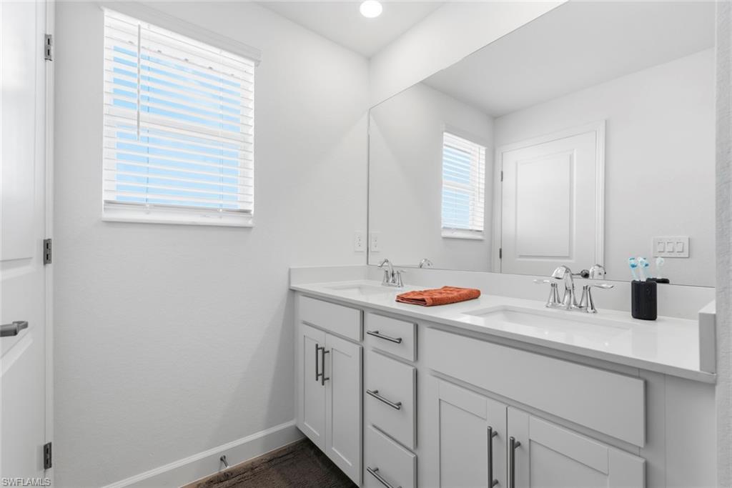 Bathroom with a long white vanity, two sinks, large mirror, and window blinds.