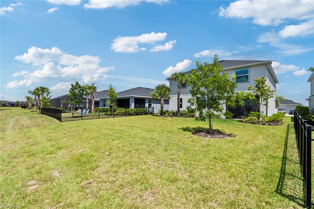 Two-story home behind a broad grassy yard, with black fencing and a screened patio.