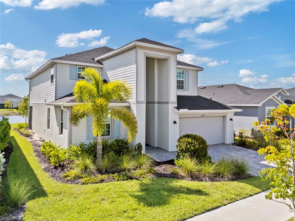 Two-story white and gray home with a front garage, palm trees, and landscaped lawn.