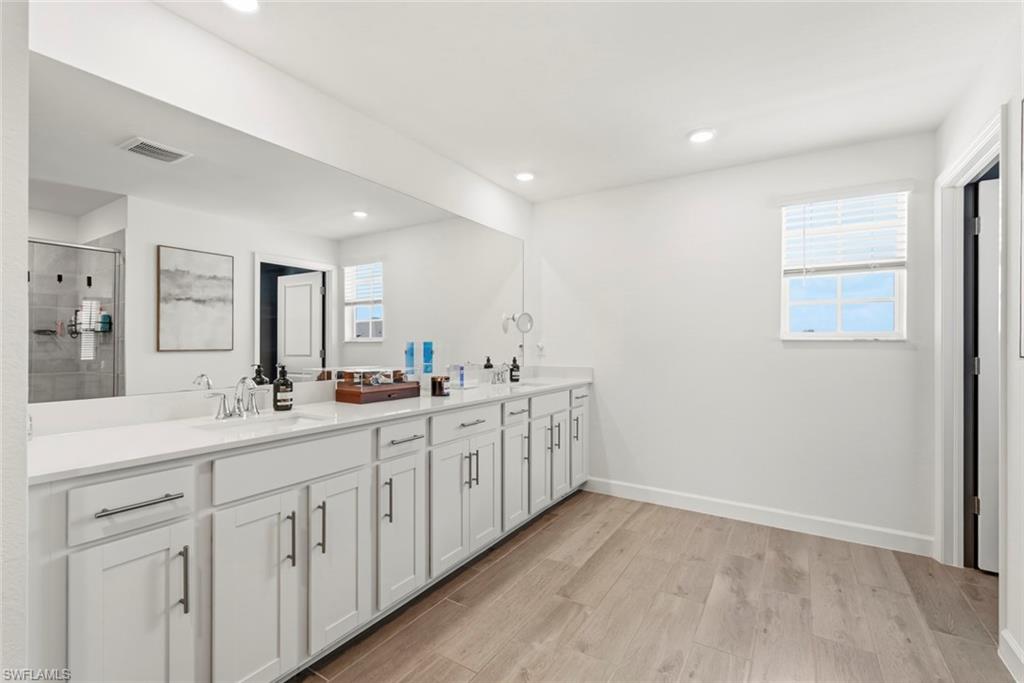 Bright bathroom with a long white vanity, large mirror, and tiled shower reflected in the glass.