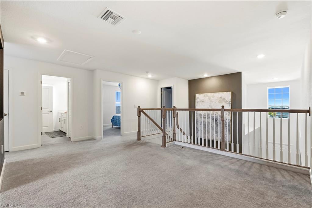 Upstairs landing with carpet, wooden stair railing, dark accent wall, and daylight through a far window.