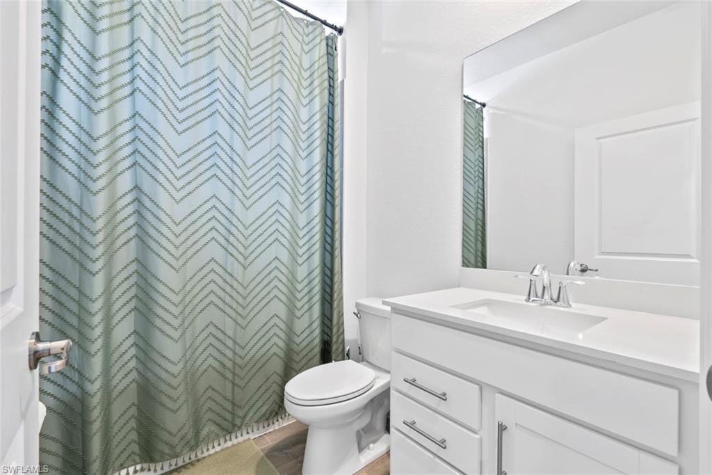 Bathroom with white vanity and toilet beside a pale green chevron shower curtain.