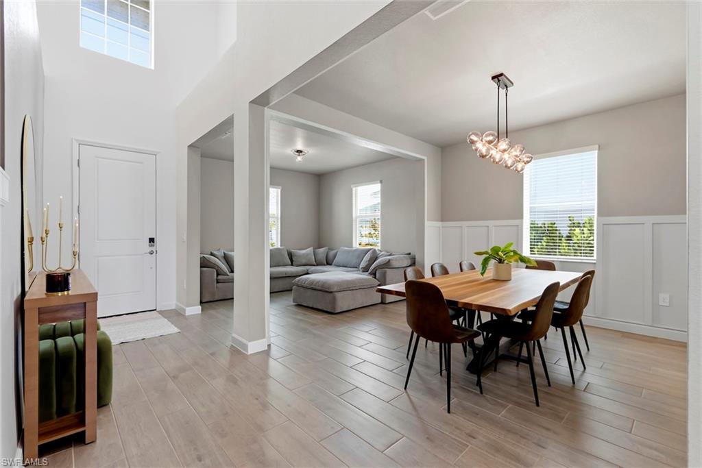 Open-plan dining and living area with a wooden table, gray sectional, and tall windows.