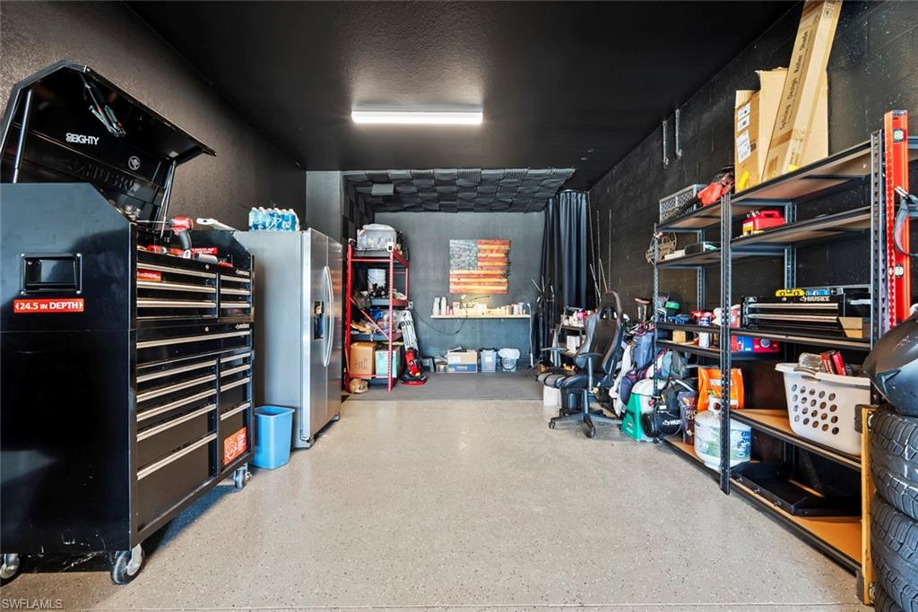 Garage workshop with black tool chests and shelving, refrigerator, and a clear central floor area.