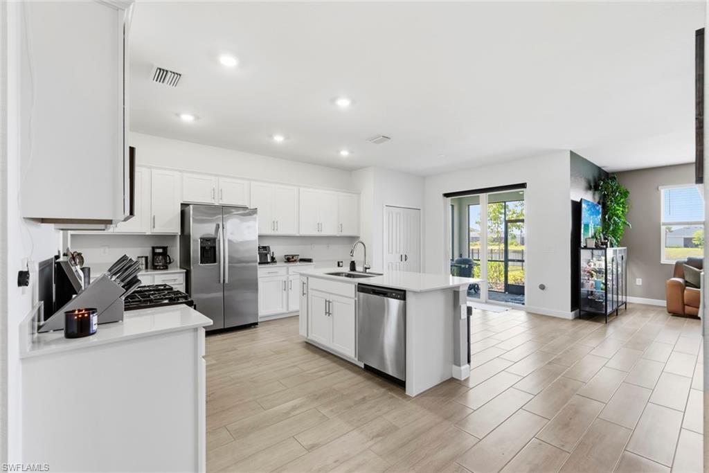 Bright kitchen with white cabinetry, stainless appliances, and a large island opening to the living area.