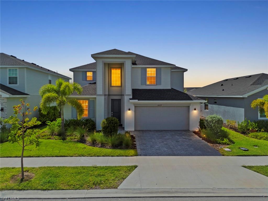 Two-story gray home with an attached garage, landscaped lawn, and glowing windows at dusk.