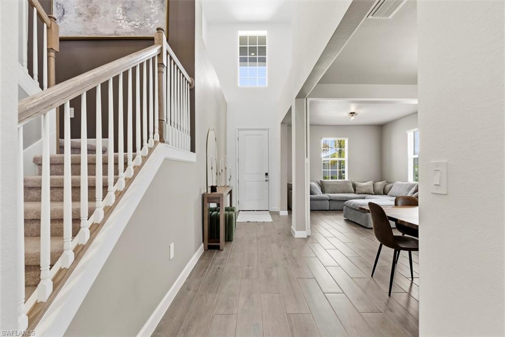 Bright foyer with carpeted staircase, high ceiling, and open connection to furnished living room.