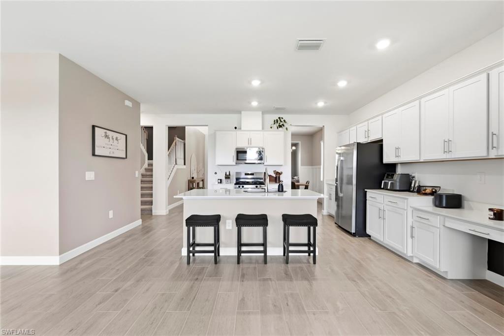 Open kitchen with white cabinets, stainless steel appliances, and a central island with three stools.