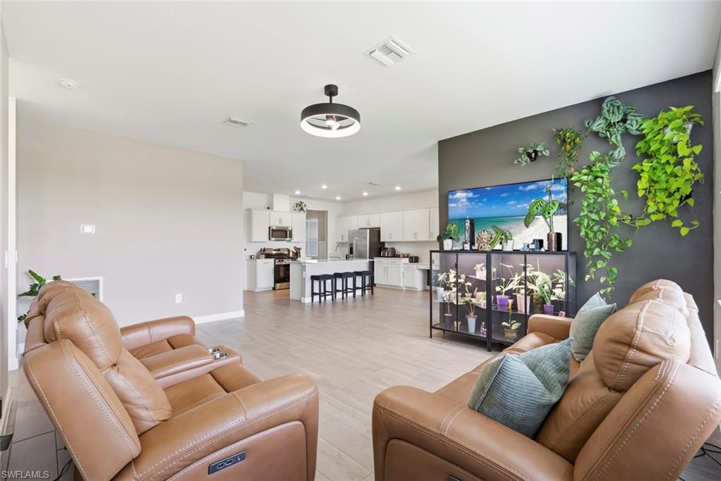 Open-plan living room with tan leather recliners, hanging plants, and a white kitchen island.