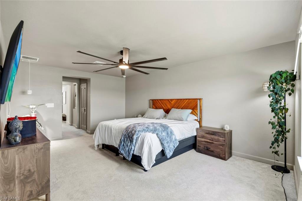Furnished bedroom with a wooden headboard, white bedding, ceiling fan, and trailing plant.