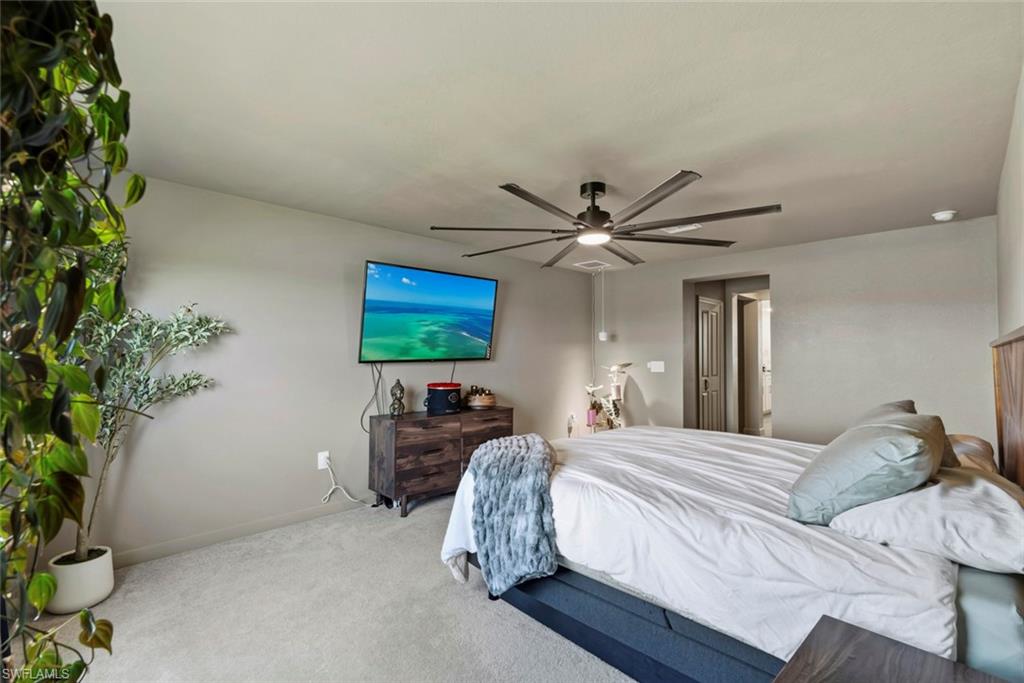 Bedroom with a white bed, dark wood dresser, wall-mounted television, and ceiling fan.