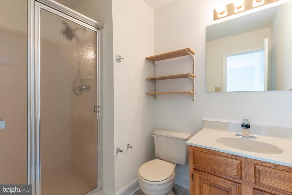 Bathroom with a frosted-glass shower, wood vanity, toilet, and open wall shelves.
