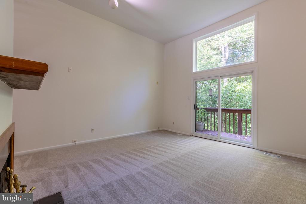 Vacant living room with beige carpet, partial fireplace, and sliding glass doors to a tree-lined deck.