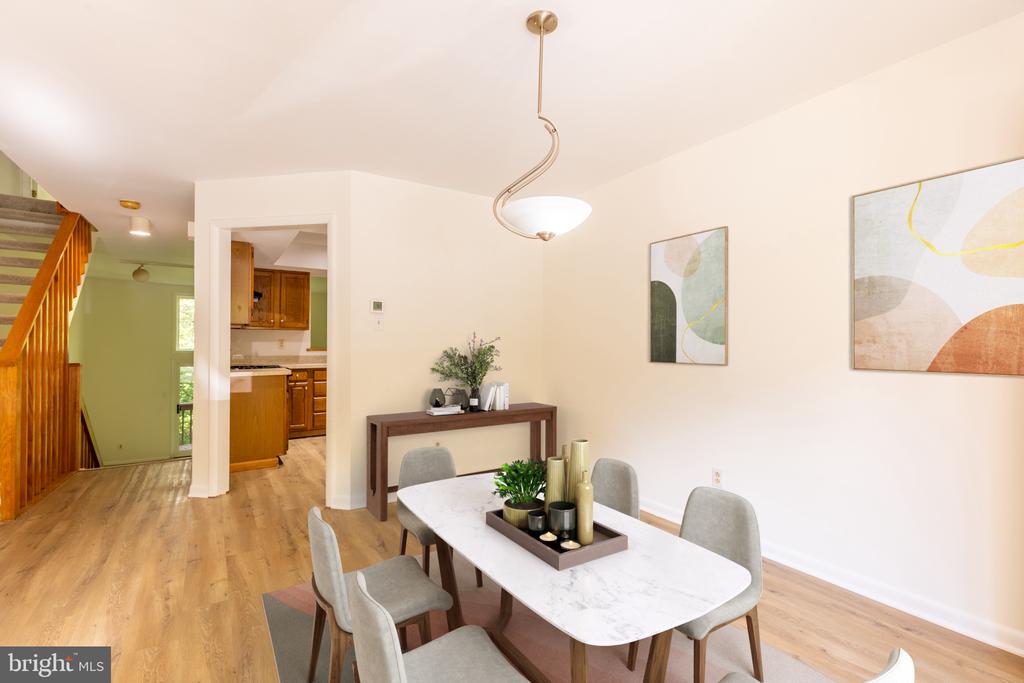 Dining room with a marble-look table and gray chairs, opening toward the kitchen and staircase.