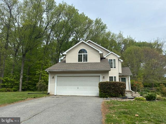 Two-story beige house with an attached garage, broad driveway, and mature trees.