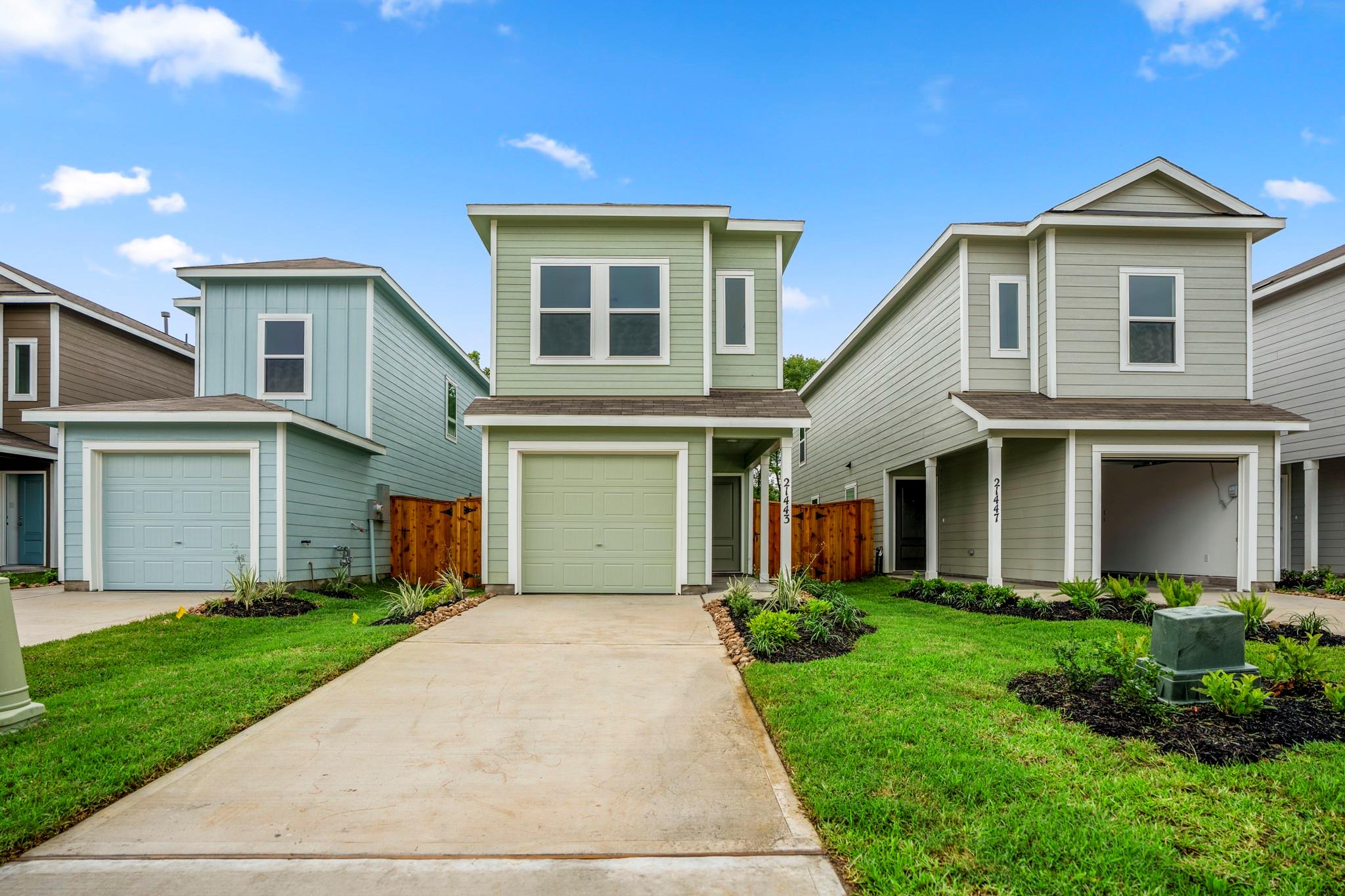 Pale green two-story home with a garage, wide driveway, and landscaped lawn.