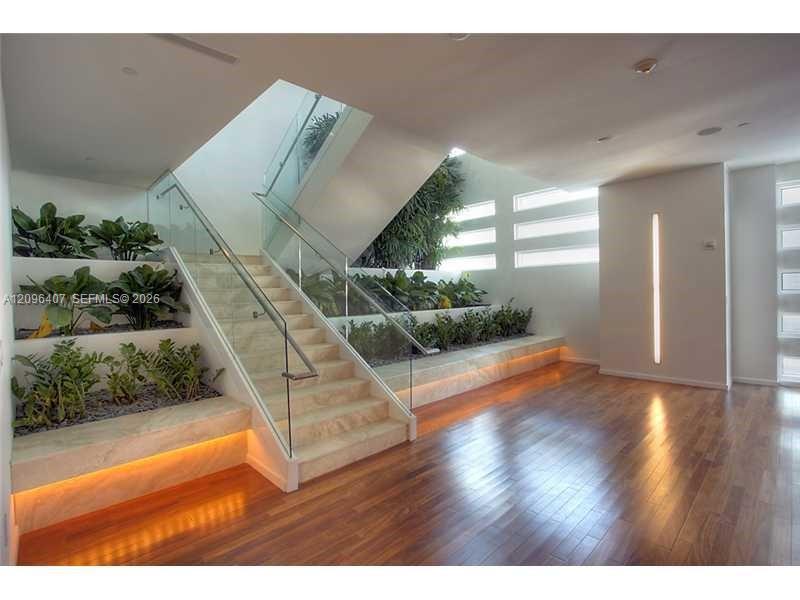 Interior staircase with glass railings, planted beds, and warm wood flooring.