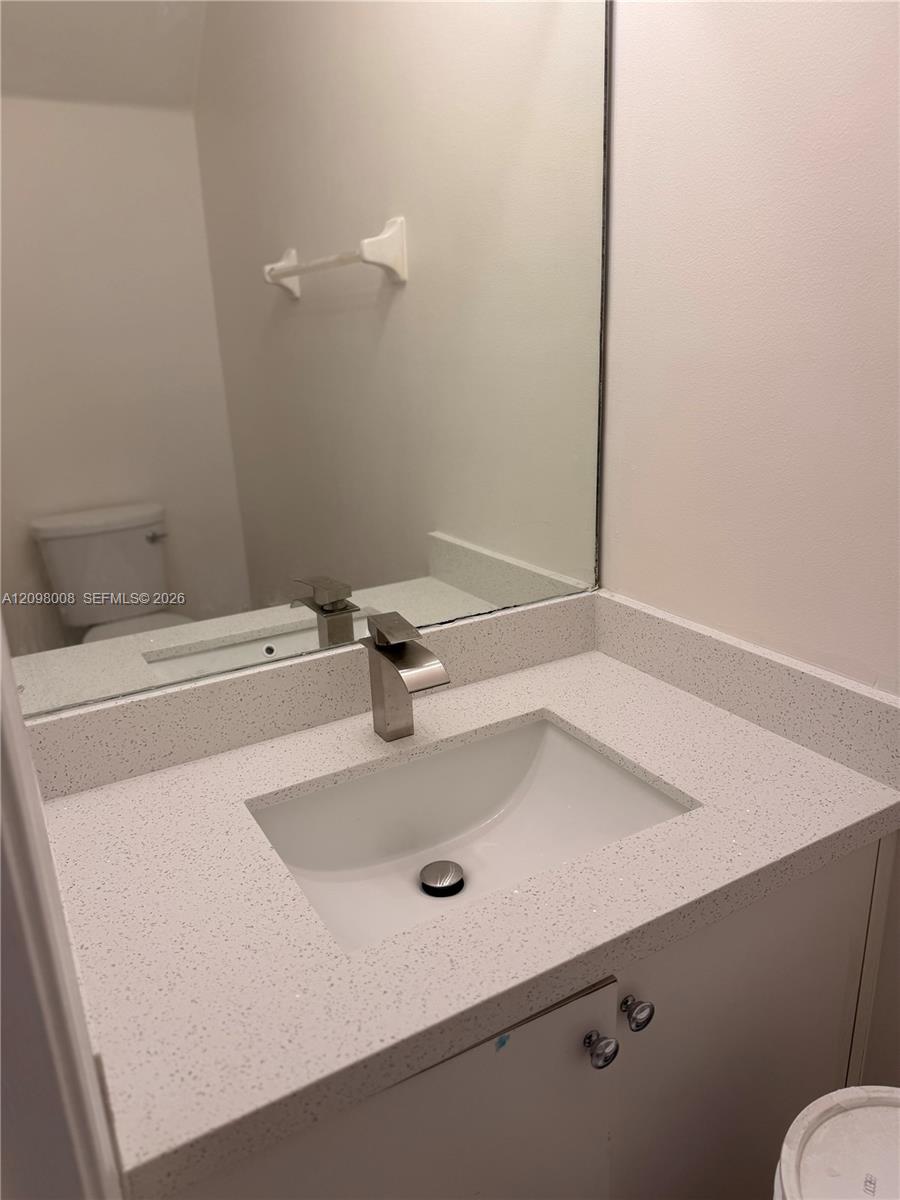 Bathroom vanity with a speckled countertop, rectangular sink, brushed metal faucet, and large mirror.