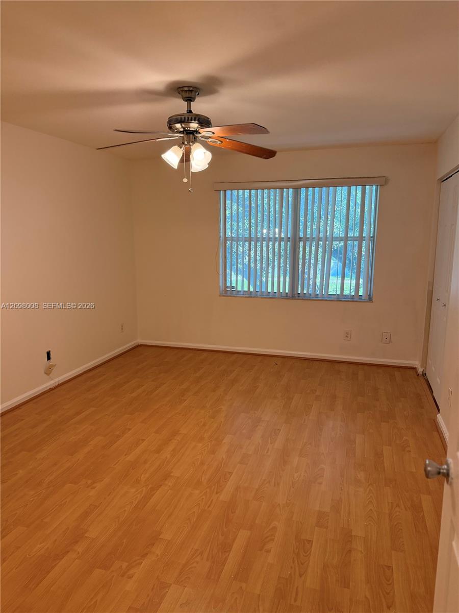 Empty room with wood-look flooring, a ceiling fan, and a window with vertical blinds.